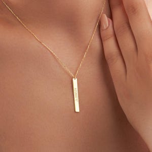 May include: A gold chain necklace with a vertical bar pendant engraved with the date "2022" and a heart symbol.