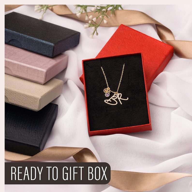 May include: A gold-colored necklace with the initials "BR" and small charms is displayed in a red gift box with a black interior. Several other gift boxes in various colors are stacked nearby. The text "READY TO GIFT BOX" is at the bottom.