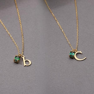 May include: Two gold-colored necklaces with delicate chains. Each necklace features a small, emerald-green rectangular gemstone and a gold letter pendant. One pendant is the letter "b", and the other is the letter "c".