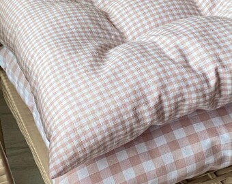 Peut inclure: Un coussin d'assise carré avec un motif à carreaux vichy rose clair et blanc. Le coussin est capitonné avec des coutures visibles créant une grille de sections rembourrées, offrant un aspect moelleux pour une assise de chaise.