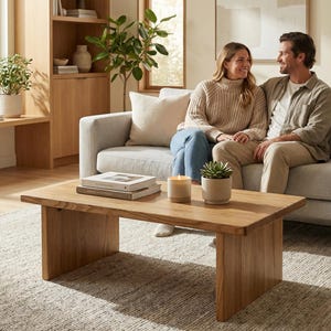 May include: A living room with a light grey sofa, a natural wood coffee table, and a textured rug. The coffee table displays books, candles, and a potted succulent. A couple sits on the sofa, creating a comfortable and inviting atmosphere.