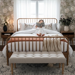 K&ouml;nnte beinhalten: Ein Schlafzimmer mit einem h&ouml;lzernen Bettrahmen, einer rostfarbenen Decke und einem cremefarbenen &Uuml;berwurf. Eine getuftete Bank befindet sich am Fu&szlig; des Bettes. Blumengemusterte Tapeten und wei&szlig;e Vorh&auml;nge umrahmen das Fenster. Eine Person liest im Bett ein Buch.