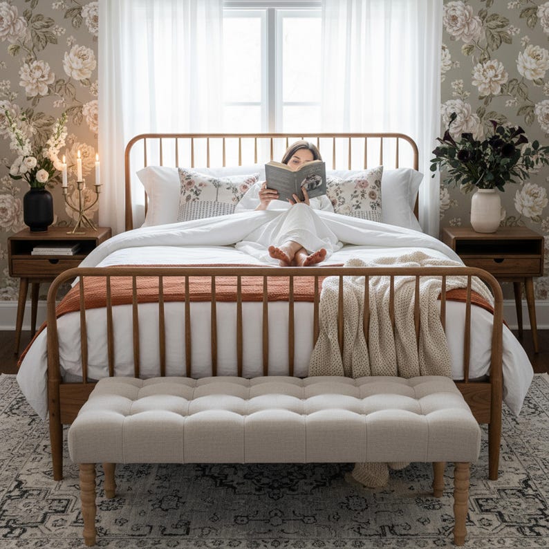 K&ouml;nnte beinhalten: Ein Schlafzimmer mit einem h&ouml;lzernen Bettrahmen, einer rostfarbenen Decke und einem cremefarbenen &Uuml;berwurf. Eine getuftete Bank befindet sich am Fu&szlig; des Bettes. Blumengemusterte Tapeten und wei&szlig;e Vorh&auml;nge umrahmen das Fenster. Eine Person liest im Bett ein Buch.