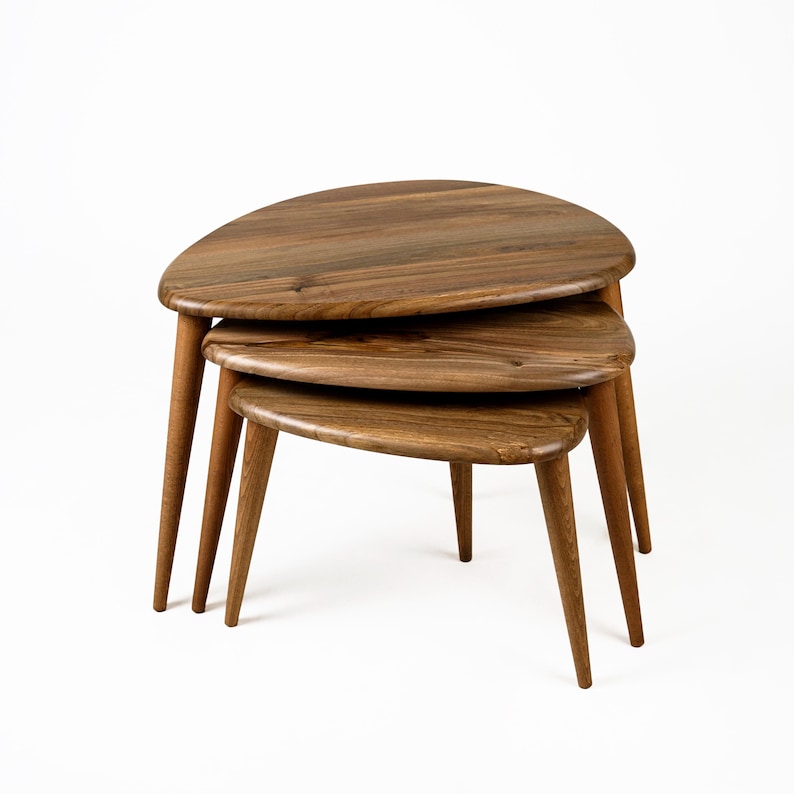 Op de afbeelding: Een set van drie nesttafels gemaakt van hout met een natuurlijke afwerking. De tafels zijn traanvormig en hebben een uniek, modern ontwerp.