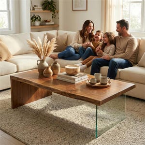 May include: A living room scene featuring a family on a cream-colored sectional sofa. A large, rectangular wooden coffee table with a glass leg holds decorative vases, a wooden bowl, books, and mugs on a tray. A beige rug covers the floor.