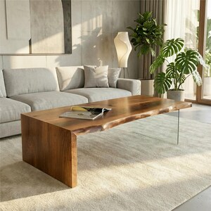 May include: A modern, rectangular coffee table with a natural wood finish and a live edge. The table has a solid wood base on one side and a clear glass leg on the other. A magazine rests on the table's surface.