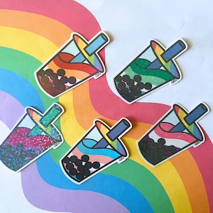 May include: A selection of bubble tea stickers in various colours. Each sticker showcases a different colour scheme, including rainbow, green, pink glitter, blue and pink, and black. The stickers are set against a rainbow background.