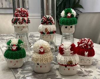 Könnte beinhalten: Sechs weiße Tassen mit verschiedenen bunten gehäkelten Weihnachtsmützen. Die Mützen haben Bommel und einige haben kleine Weihnachtsmann-Figuren oben drauf.