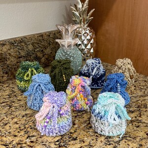 May include: A collection of nine crocheted drawstring bags in various colors, including green, blue, purple, and pink. The bags are made with different stitch patterns and have decorative beads.