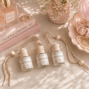 May include: Three small glass car air freshener bottles with wooden caps and braided hanging cords. Each bottle features a white label with the text Delica Candle Co. and Opulent Petals, decorated with a subtle botanical line art illustration.