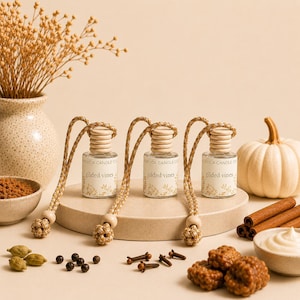 May include: Three small glass car air freshener bottles with wooden caps and braided hanging cords. Each bottle features a white label with the text "Adelica Candle Co." and "Gilded Vines" printed above a botanical illustration in a tan color.