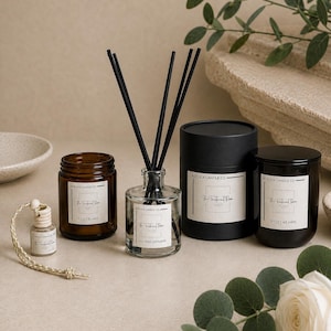 May include: A collection of home fragrance products including a small hanging car diffuser, an amber glass candle jar, a clear glass reed diffuser with black reeds, and a black candle jar with a matching cylindrical box, all labeled Adelica Candle Co.