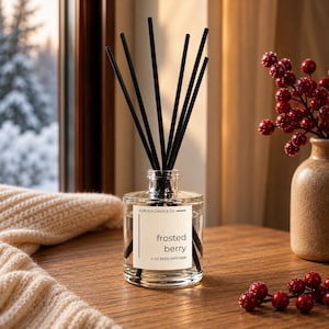 May include: A clear glass reed diffuser bottle with a white label reading Adelica Candle Co frosted berry 4 oz reed diffuser. The bottle contains clear liquid and several thin black reeds extending upwards from the narrow neck opening.