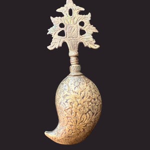 May include: A gold-coloured metal bottle stopper with an ornate design. The stopper is shaped like a teardrop with a decorative top.