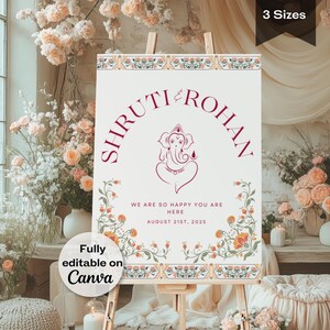 May include: A white wedding welcome sign with a floral border and a burgundy text that reads "Shruti & Rohan". The sign also features a burgundy illustration of the Hindu deity Ganesha. The text below the illustration reads "We are so happy you are here August 21st, 2025".