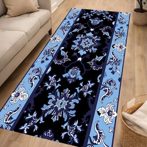 Op de afbeelding: Een rechthoekige loper met een zwart middenpaneel versierd met complexe bloemen- en rankpatronen in lichtblauw, marineblauw en wit. Het kleed is omlijst door twee lichtblauwe randen die zijn gedecoreerd met witte en marineblauwe bloemmotieven.