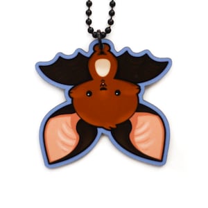 Puede incluir: Un murci&eacute;lago marr&oacute;n con orejas rosas colgando boca abajo de un collar de cadena negra. El murci&eacute;lago es de estilo de dibujos animados y tiene ojos grandes y redondos. El collar es de metal.