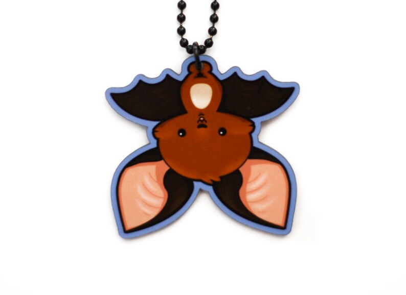 Puede incluir: Un murci&eacute;lago marr&oacute;n con orejas rosas colgando boca abajo de un collar de cadena negra. El murci&eacute;lago es de estilo de dibujos animados y tiene ojos grandes y redondos. El collar es de metal.