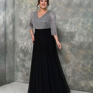 May include: A formal dress featuring a silver, sequined top with a V-neck and three-quarter sleeves. The skirt is a flowing, floor-length black fabric. The dress has a defined waistline and is suitable for special occasions.