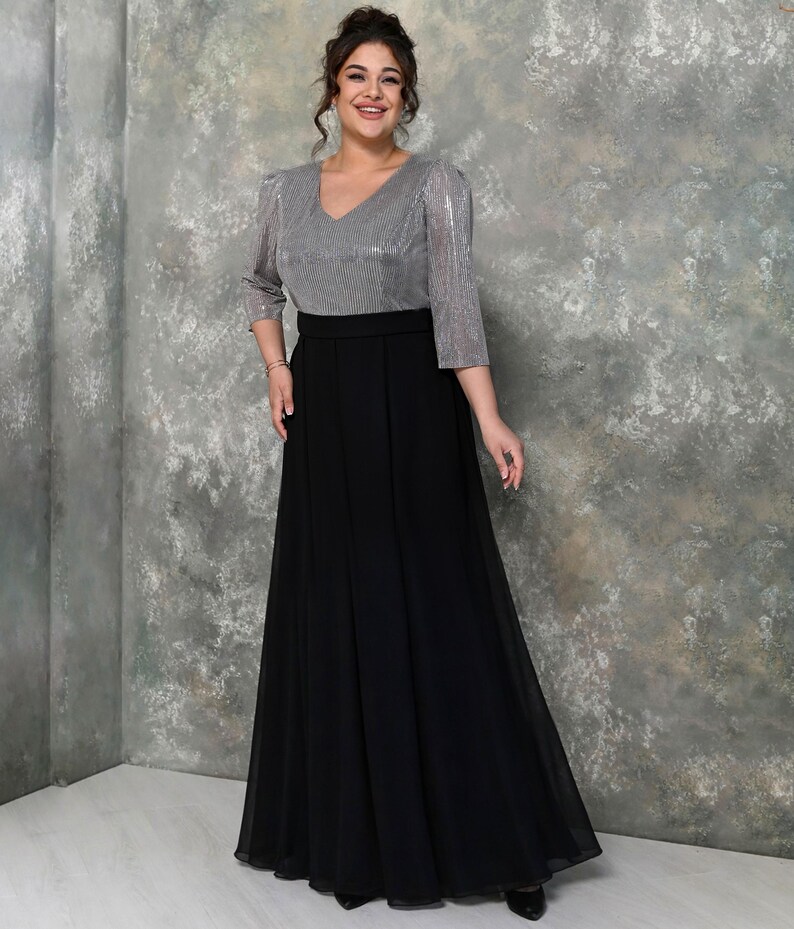May include: A formal dress featuring a silver, sequined top with a V-neck and three-quarter sleeves. The skirt is a flowing, floor-length black fabric. The dress has a defined waistline and is suitable for special occasions.