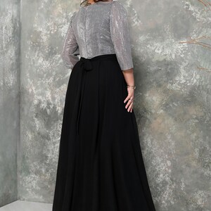 May include: A formal dress featuring a silver sequined top with three-quarter sleeves and a long, flowing black skirt. The dress has a tie at the waist and is paired with black high-heeled shoes. The background is a textured gray wall.