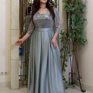 May include: A formal, floor-length gown in a soft, silvery-blue hue. The bodice features a V-neck and shimmering sequins, with three-quarter sleeves. The skirt flows gracefully from the waist. The dress is suitable for special occasions.