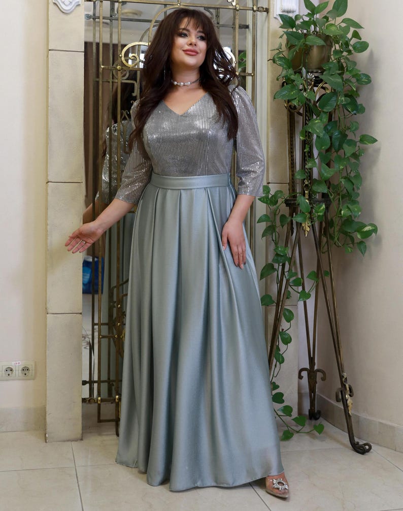 May include: A formal, floor-length gown in a soft, silvery-blue hue. The bodice features a V-neck and shimmering sequins, with three-quarter sleeves. The skirt flows gracefully from the waist. The dress is suitable for special occasions.