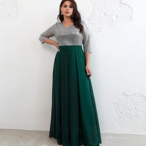 May include: A formal dress featuring a silver sequined bodice with a V-neck and three-quarter sleeves. The skirt is a flowing, floor-length emerald green. The dress has a high waistline and is suitable for special occasions.