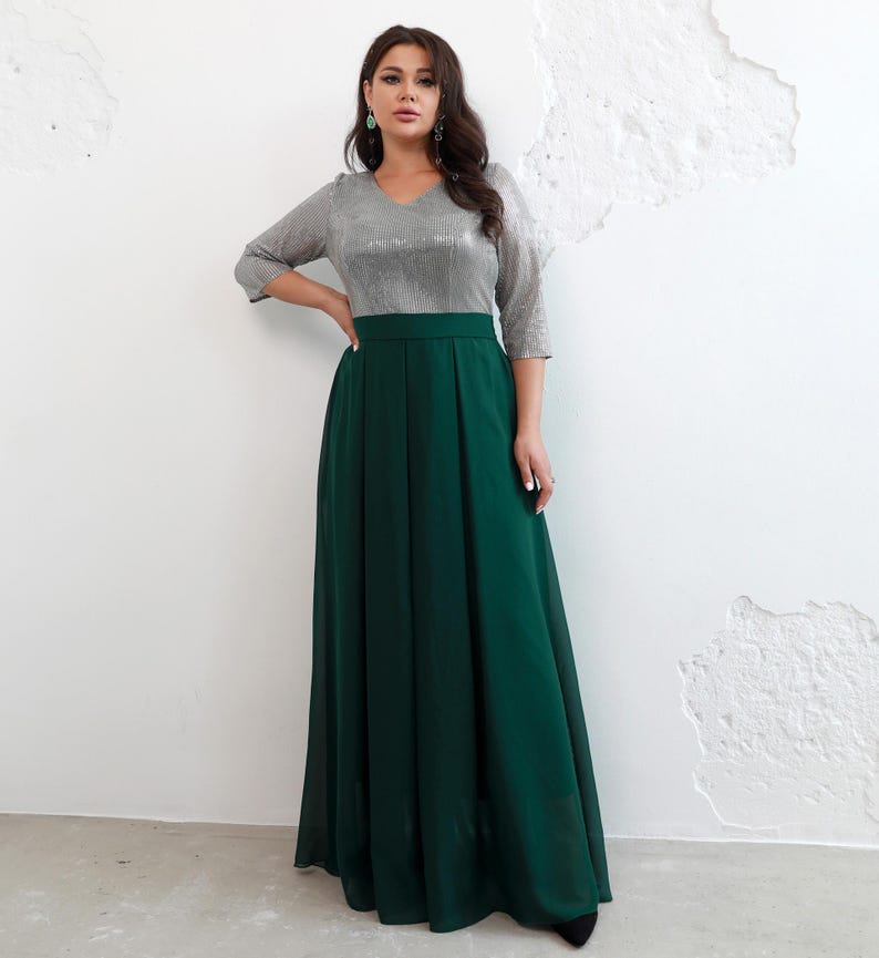 May include: A formal dress featuring a silver sequined bodice with a V-neck and three-quarter sleeves. The skirt is a flowing, floor-length emerald green. The dress has a high waistline and is suitable for special occasions.