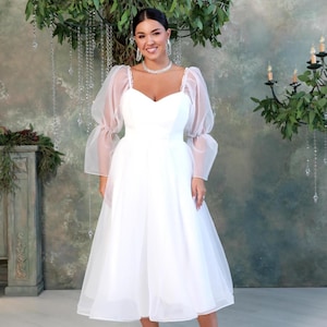 Biała, skromna suknia ślubna z gorsetem i prześwitującymi bufiastymi rękawami. Romantyczna, jesienna suknia ślubna midi.