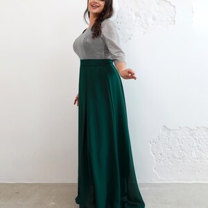 May include: A long, emerald green skirt paired with a silver and gray striped top. The top has three-quarter sleeves and a scoop neckline. The skirt is high-waisted and flows to the floor. The outfit is suitable for formal events.
