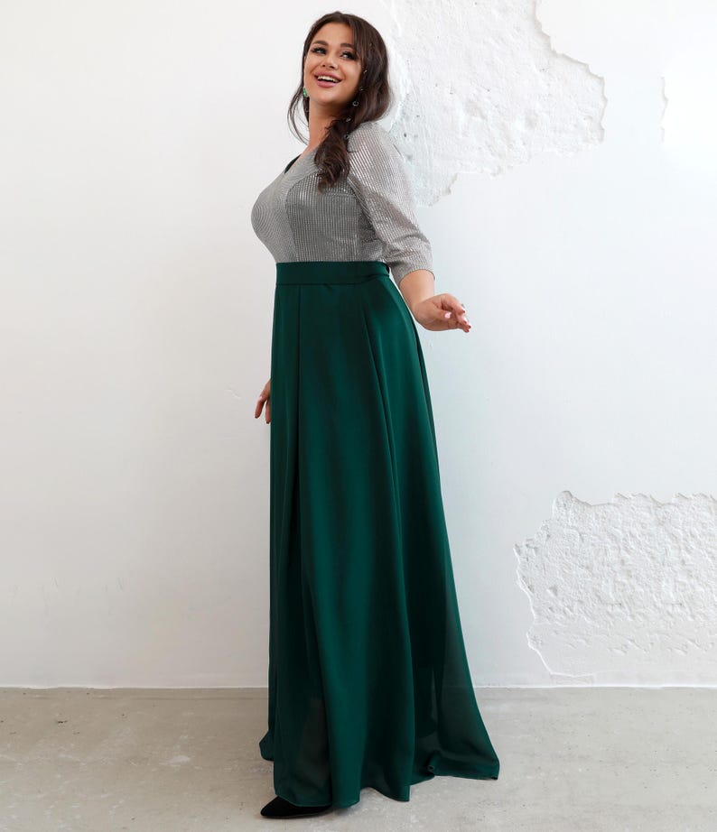 May include: A long, emerald green skirt paired with a silver and gray striped top. The top has three-quarter sleeves and a scoop neckline. The skirt is high-waisted and flows to the floor. The outfit is suitable for formal events.