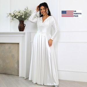 May include: A long, white satin dress with long sleeves and a V-neck. The dress has a fitted bodice and a flowing skirt. The image also shows a vase of white flowers and the text "US Tariffs Paid".