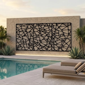 May include: A black metal decorative wall panel with a geometric, abstract design. The panel is mounted on a textured stone wall, with a pool and lounge chairs in the foreground. The panel is approximately 10 feet wide.