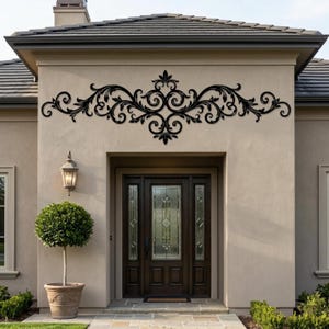 Może przedstawiać: Czarny, metalowy element architektoniczny, zamontowany nad ciemnymi drewnianymi drzwiami. Element dekoracyjny ma symetryczny wzór z wirujących wzorów i kształtów liści, dodając elegancji do zewnętrznej części domu.