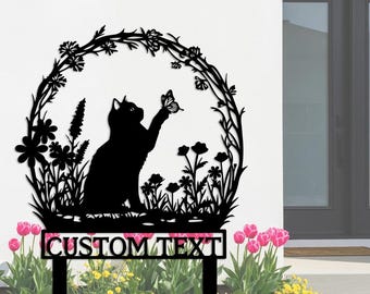 May include: Black metal garden stake featuring a cat reaching for a butterfly within a floral wreath. The design includes flowers and foliage, with the words "CUSTOM TEXT" at the base. The stake is set in a garden with pink tulips and yellow flowers.