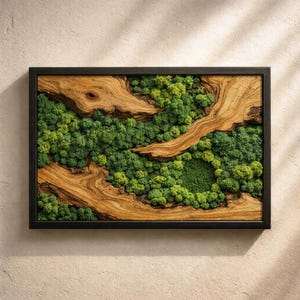 Op de afbeelding: Een rechthoekig, ingelijst kunstwerk met een natuurlijk ontwerp. Het combineert lichtbruine houten elementen met levendig groen mos, waardoor een gelaagd, driedimensionaal effect ontstaat. De zwarte lijst zorgt voor een strakke rand.