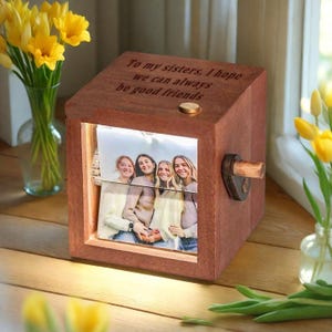 May include: A wooden photo cube with a picture of four women. The cube has a light inside and a wooden handle. The top of the cube has the inscription: "To my sisters, I hope we can always be good friends."