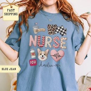 May include: Blue jean colored t-shirt with a graphic design featuring the word "NURSE" in patchwork letters, a coffee cup, a corgi, a heart, and the name "Amilia". The shirt also has the text "Coffee break" and "ICU".