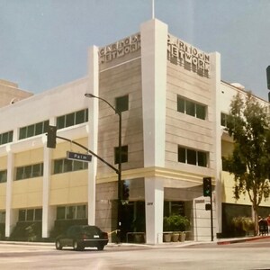 May include: A beige building with a sign that reads "Cartoon Network" and "Cartoon Network" on the front. The building has large windows and a yellow trim. There is a palm tree in front of the building.