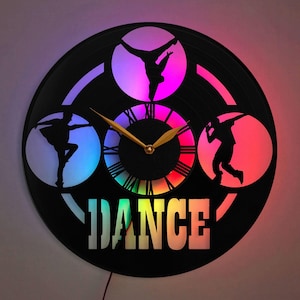 May include: A black vinyl record clock with a rainbow-colored clock face and three silhouettes of dancers. The clock face has Roman numerals and the word "DANCE" is printed below the clock face.