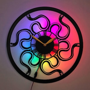May include: A black and white clock with a snake design. The clock face is surrounded by a rainbow of colors. The clock has Roman numerals and a gold-colored hour and minute hand.