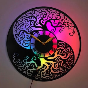 以下が含まれることがあります： 木製のデザインの白黒の時計。時計の文字盤は虹色に光っています。時計は陰陽のデザインです。