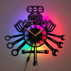 May include: A black metal wall clock with a rainbow LED light design. The clock features a stylized engine design with wrenches and other tools as the clock hands.