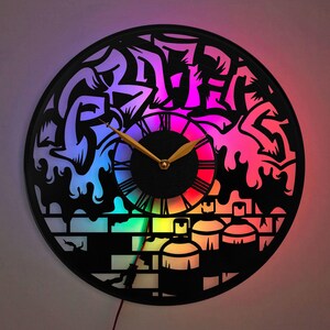 May include: A black vinyl record clock with a graffiti design featuring the word "Graffiti" in a stylized font. The clock has a rainbow LED light effect and features spray paint cans and a brick wall design.