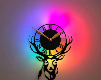 May include: A black deer head silhouette clock with Roman numeral markings and gold hands. The clock is illuminated with a rainbow-colored light.