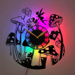 以下が含まれることがあります： 虹色の背景を持つ白黒の時計。時計はキノコの形をしており、妖精と花で囲まれています。