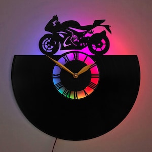 Könnte beinhalten: Eine schwarze Schallplattenuhr mit einem regenbogenfarbenen Zifferblatt und einer Silhouette eines Motorrads obenauf. Die Uhr wird mit bunten LED-Lichtern beleuchtet.