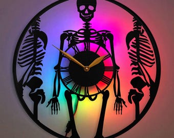 May include: A black skeleton clock with a rainbow LED light behind it. The clock has a gold-coloured hour and minute hand. The clock is round and has a black frame.