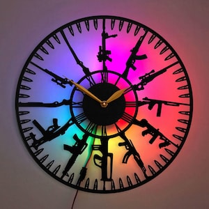 May include: A black clock with a rainbow-coloured background. The clock face is surrounded by a ring of bullet-shaped outlines. The clock hands are gold and black. The clock is made of metal and has a modern design.